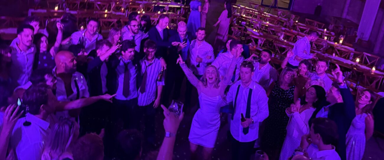 Packed Wedding Dancefloor | Mr Beats Essex DJ Packed wedding reception dancefloor with guests raising their hands under pink and purple DJ lighting